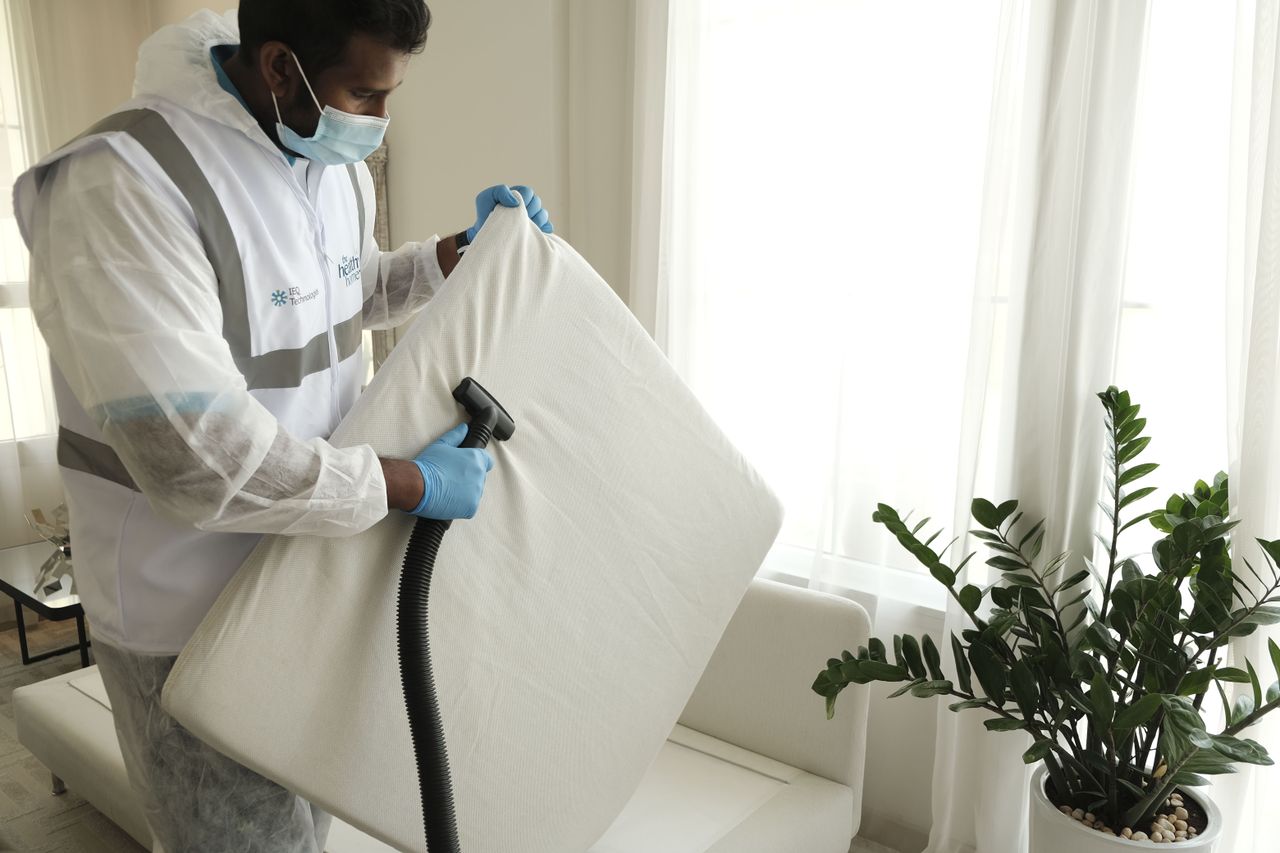 who-we-are Man in protective gear vacuuming a mattress in a modern home interior.