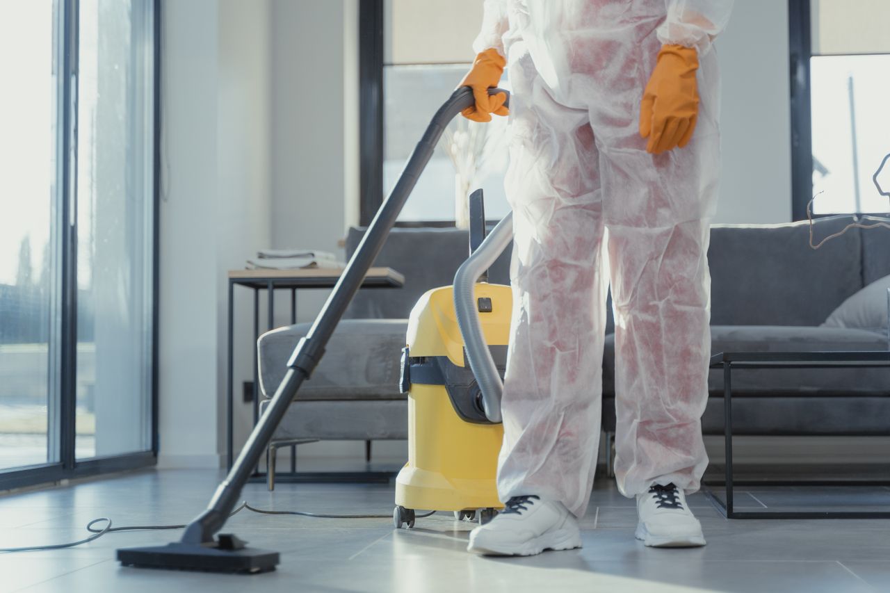 about-us A cleaner in protective coveralls and gloves vacuuming a modern living room.
